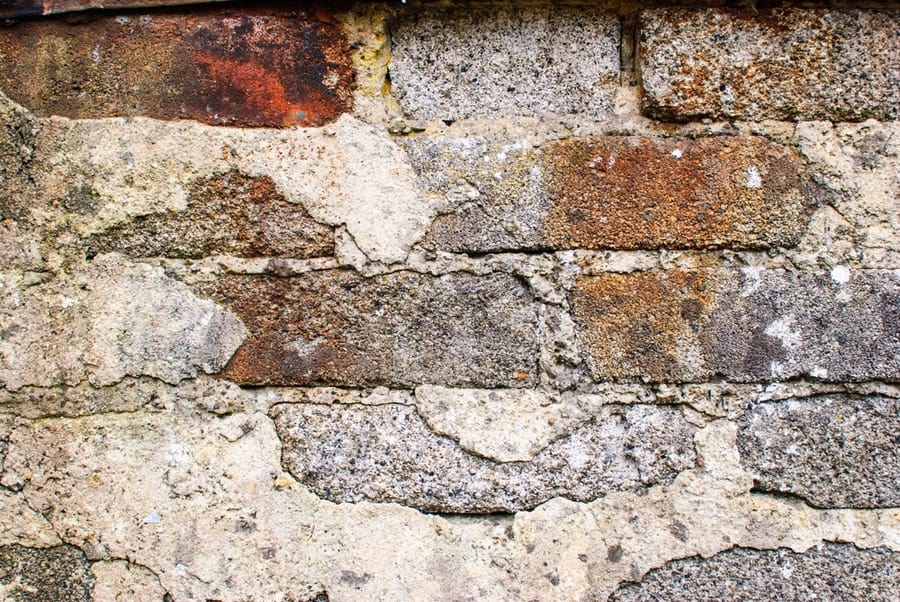 An Old Rough Rendered Gray Cement Brick Wall With Rust Stains