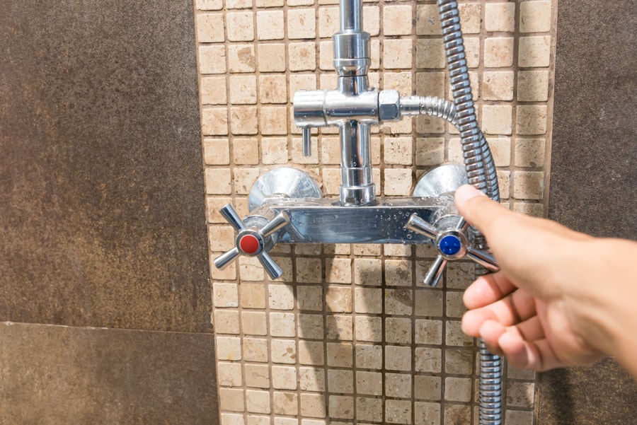 Close Up Hand Turning Blue Or Cool Shower Faucet In Bathroom.