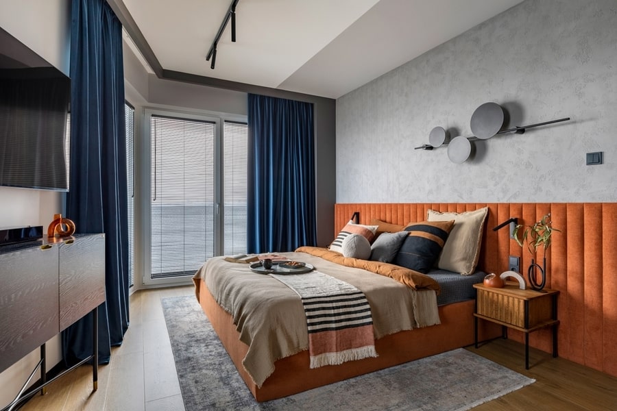 Interior Design Of Elegant Bedroom With Big Orange Bed, Beige And Grey Bedclothes, Blue Curtain, Rug, Modern Lamp, Night Stand, Vase With Dried Flowers And Personal Accessories.