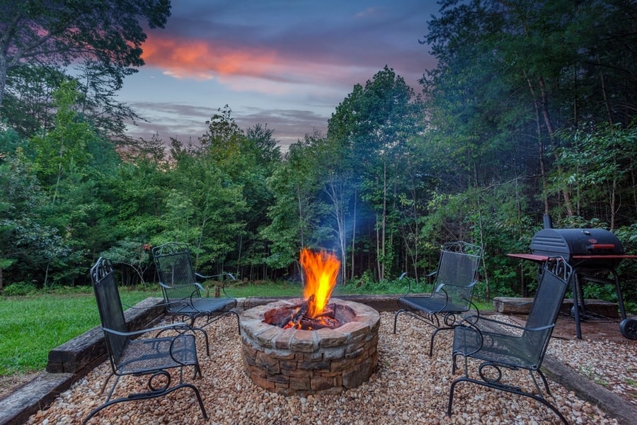 Roaring Fire In A Stone Firepit With Wood Logs And Surrounded By Trees At Dusk In A Backyard