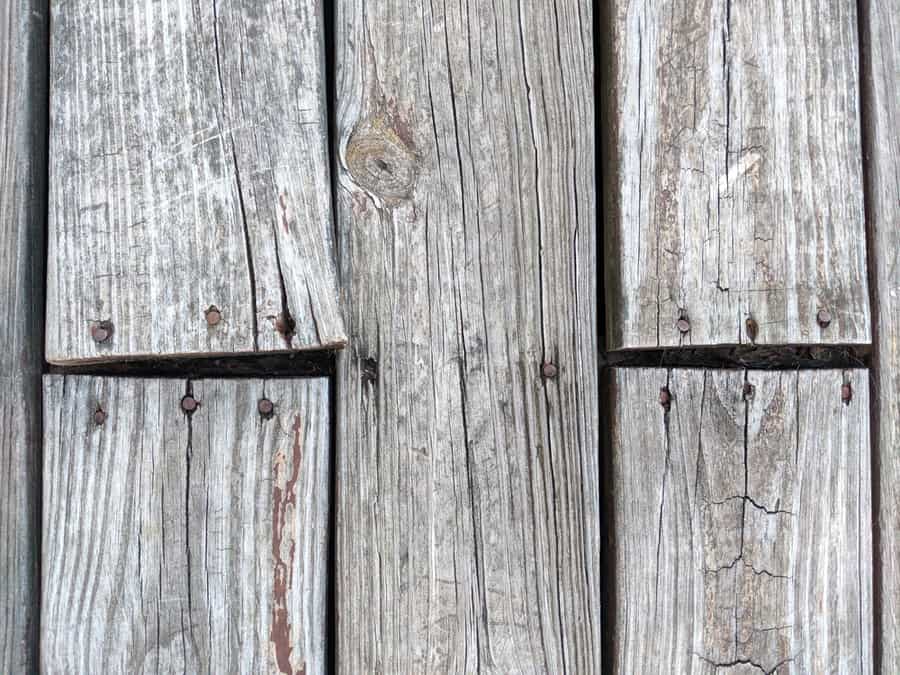 Top View Of Wooden Deck Floor Boards Coming Up, Warped And Weathered, Needing To Be Nailed And Repaired