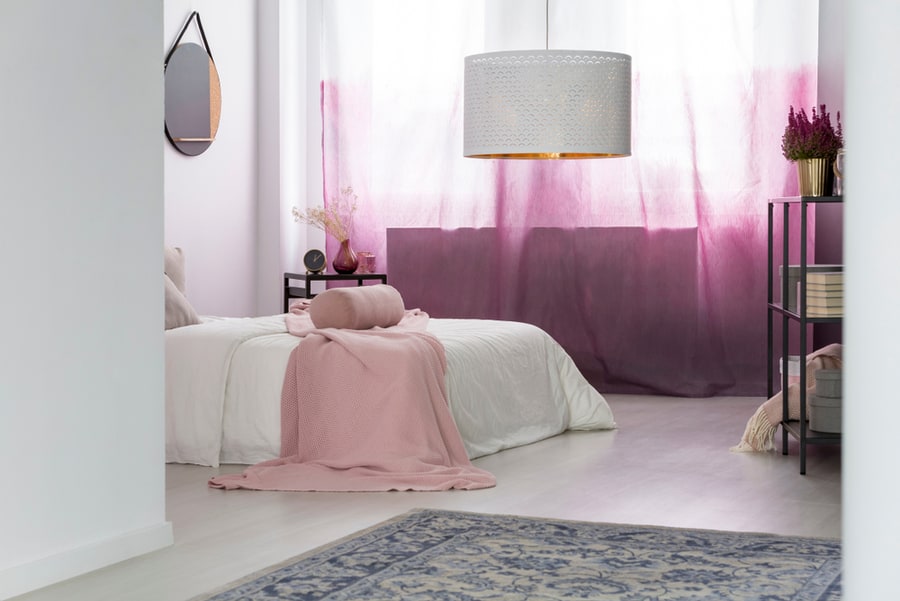 White Lamp Above Grey Carpet In Bedroom With Pink Curtains And Mirror Above Bed With Blanket