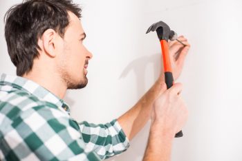 A Man Hammering A Nail On The Wall