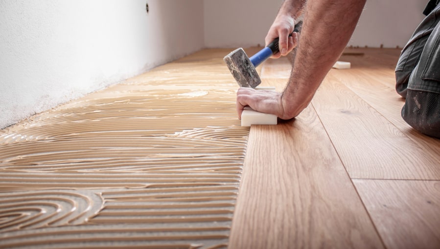 Craftsman Lays Parquet Floor And Spreads The Glue On The Screed And Beats The Floorboards With The Hammer And The Block