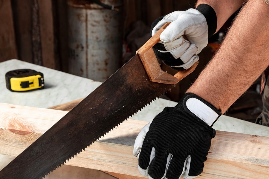 A Man Cuts A Wooden Beam Using A Handsaw