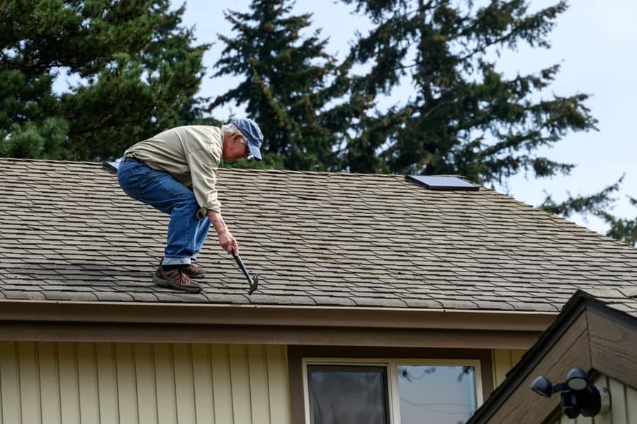 Senior Man Standing On A House Roof With A Hammer